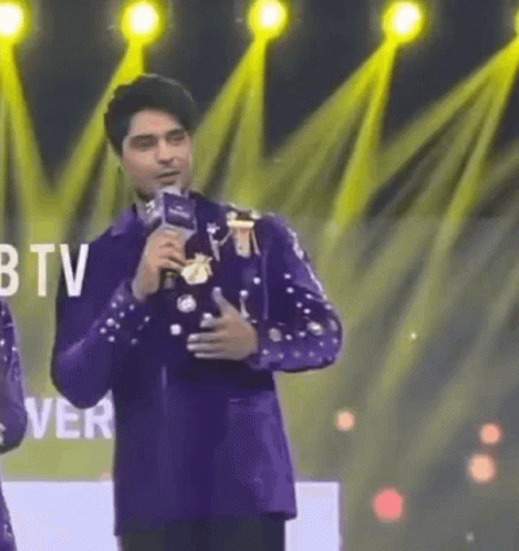 Man in Purple Suit Holding Microphone in Front of BTV Logo