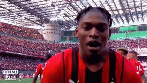 Man in Red and Black Striped Shirt in Front of Futball Stadium