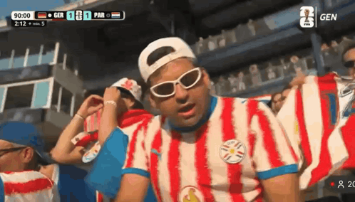 Man in Red and White Striped Shirt in Front of Scoreboard