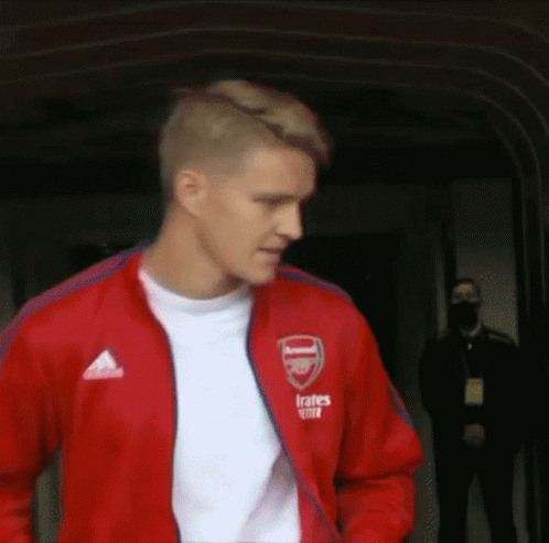Man In Red Jacket And White Shirt Walking Down Hallway GIF