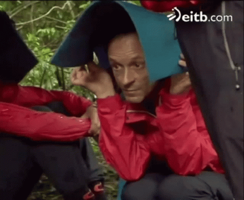 Man in Red Jacket Covering Head With Blue Blanket in Rain