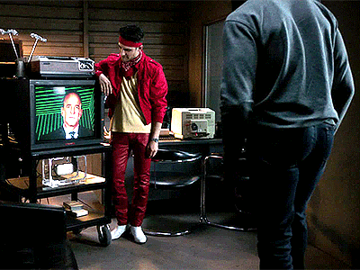 Man in Red Jacket Watching Man on TV