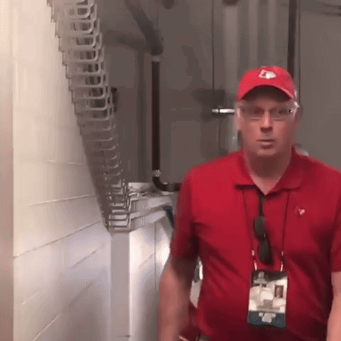 Man in Red Shirt and Red Hat With Letter E Standing in Hallway
