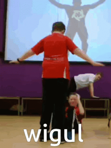 Man in Red Shirt Doing Handstand in Front of Screen Saying Wigui