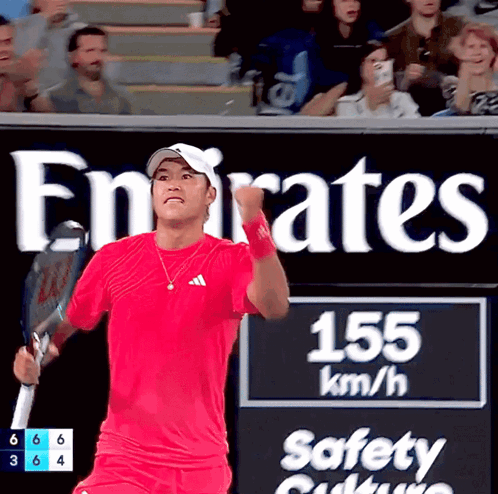 Man in Red Shirt Holding Tennis Racquet in Front of Emirates Sign