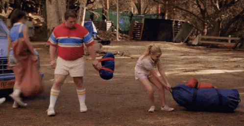 Man in Red Shirt Pushing Woman Pulling Bag