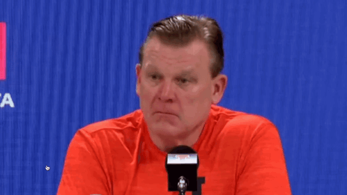 Man in Red Shirt Sitting at Microphone Looking at Camera