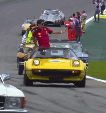Man in Red Shirt Waves to Yellow Car on Track