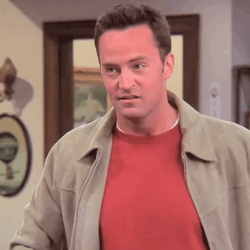 Man in Red Sweater and Tan Jacket Standing in Front of Door