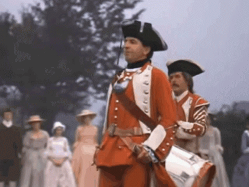 Man in Red Uniform Holding Drum in Front of Crowd