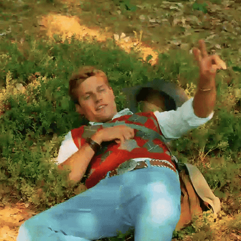 Man In Red Vest And Blue Jeans Laying In Grass GIF