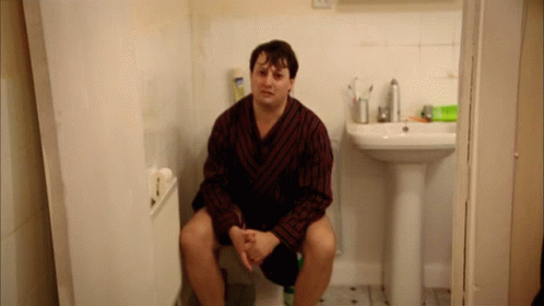 Man in Robe on Toilet Beside Bathroom Sink
