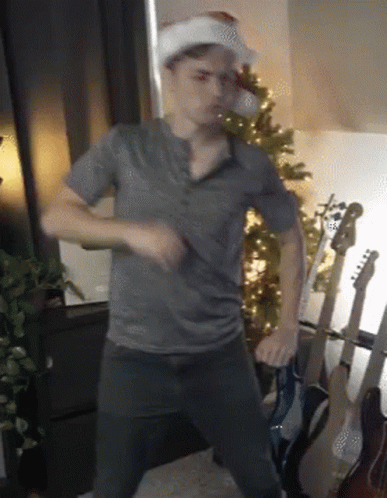 Man In Santa Hat Dancing By Christmas Tree GIF
