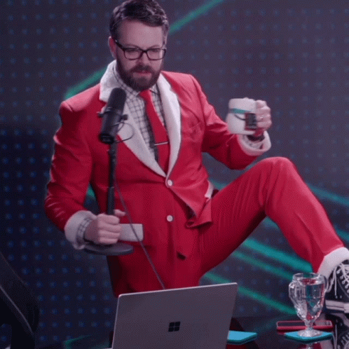 Man in Santa Suit Sitting at Laptop Holding Cup