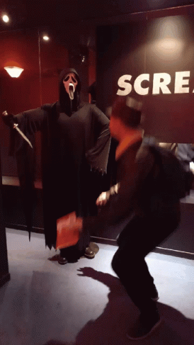 Man In Scream Costume Standing In Front Of Scream Sign GIF