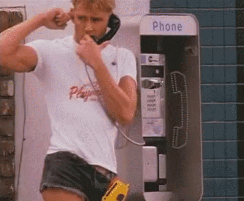 Man in Shorts Talking on Payphone