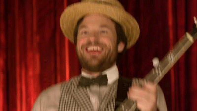 Man in Straw Hat and Bow Tie Holding Guitar in Front of Red Curtain