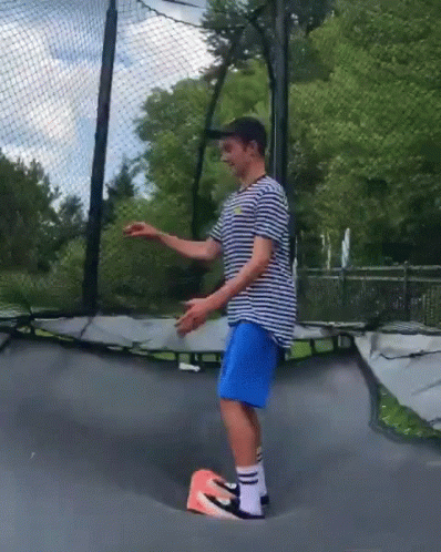 Man in Striped Shirt, Blue Shorts, and Nike Shoes on Trampoline