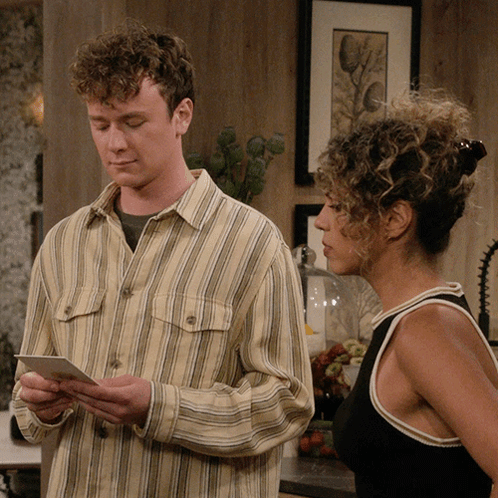 Man In Striped Shirt Looking At Paper Next To Woman GIF