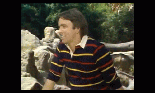 Man in Striped Shirt Next to Pile of Rocks