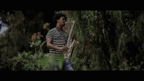 Man In Striped Shirt Playing Saxophone Outside GIF