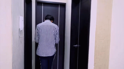 Man in Striped Shirt Standing in Front of Black Door