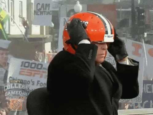 Man in Suit Adjusts Helmet in Front of Cam Newton Sign