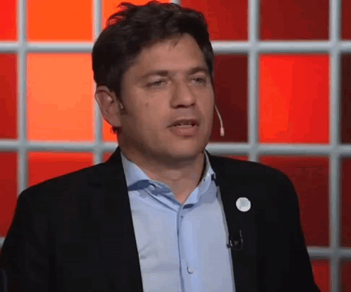 Man in Suit and Blue Shirt Talking Into Microphone in Front of Red Wall