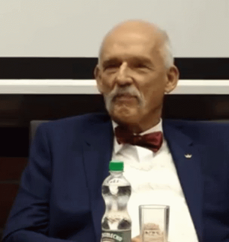 Man in Suit and Bow Tie Sitting at Table With Aquafina Water