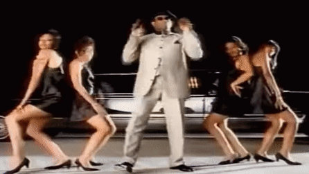 Man in Suit and Hat Dancing With Three Women in Black Dresses in Front of a Car