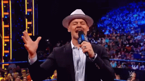 Man in Suit and Hat Holding Microphone Amid Crowd