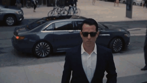 Man In Suit And Sunglasses Walking Past Car GIF