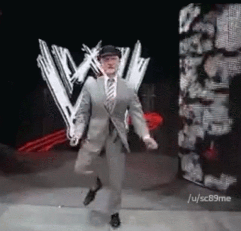 Man in Suit and Tie Dancing in Front of Wrestling Logo