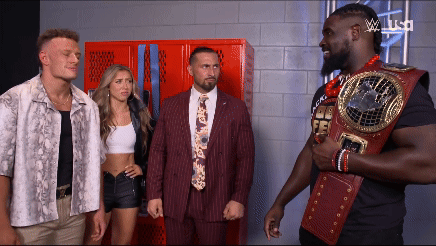 Man in Suit and Tie Holding Championship Belt Beside Two Men