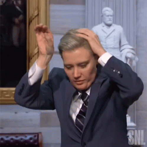 Man In Suit And Tie Holding Head Next To SNL Statue GIF