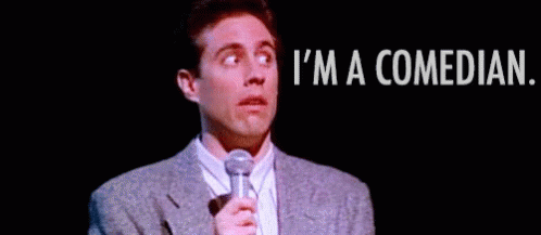 Man In Suit And Tie Holding Microphone Saying I'm A Comedian GIF