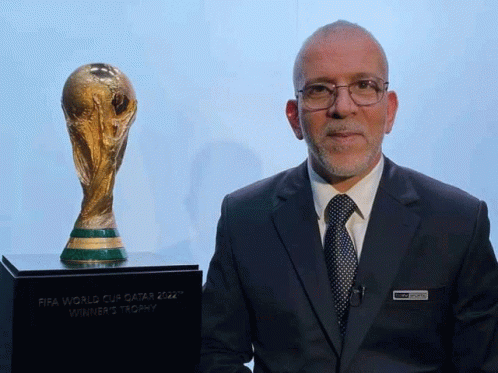 Man in Suit and Tie Next to FIFA World Cup Qatar 2022 Winner's Trophy