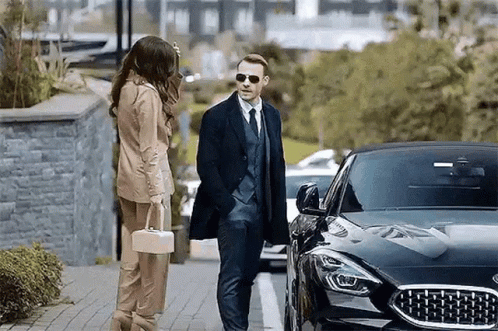 Man In Suit And Tie Next To Woman With Purse GIF