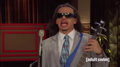 Man In Suit And Tie Singing Into Microphone Holding Adult Swim Guitar GIF