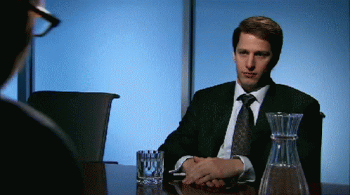 Man in Suit and Tie Sitting at Table With Glass of Water and Decanter