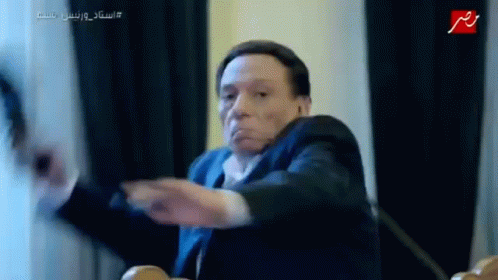 Man In Suit And Tie Sitting At Table With Hands Outstretched GIF