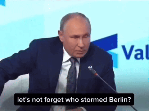 Man In Suit And Tie Speaking Into Microphone Saying Let's Not Forget Who Stormed Berlin GIF
