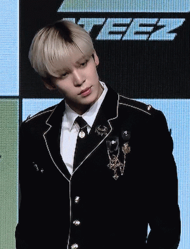 Man in Suit and Tie Standing Before Screen Saying Tbz