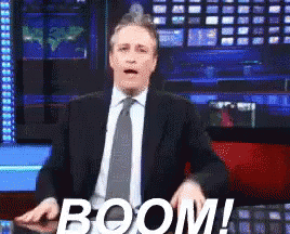 Man In Suit And Tie Standing Beside Boom Sign GIF