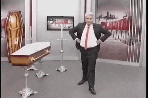 Man In Suit And Tie Standing By Coffin And TV GIF