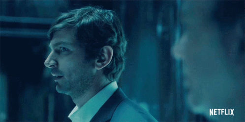 Man In Suit And White Shirt Standing In Dark Room With Netflix Logo GIF