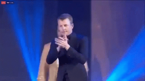 Man in Suit Applauding with Another Man Behind