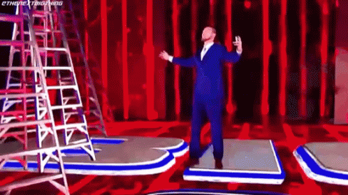 Man In Suit Arms Outstretched On Red Stage GIF