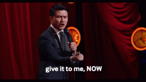 Man in Suit at Mic Says Give It to Me Now