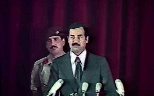 Man In Suit At Microphones With Military Behind GIF